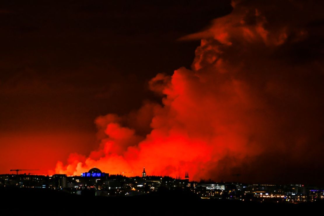 El horizonte de Reykjavik tiene como telón de fondo un cielo de color naranja debido a la lava fundida que fluye desde una fisura en la península de Reykjanes al norte de la ciudad evacuada de Grindavik, en el oeste de Islandia, el 16 de marzo de 2024.