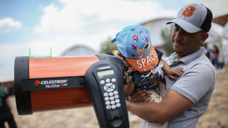 Un hombre carga a su hijo mientras mira por un telescopio durante el XXVII Festival de Astronomía que reúne a profesionales y entusiastas de la astronomía para compartir conocimientos sobre el universo en Villa de Leyva, Colombia, el 17 de marzo de 2024.