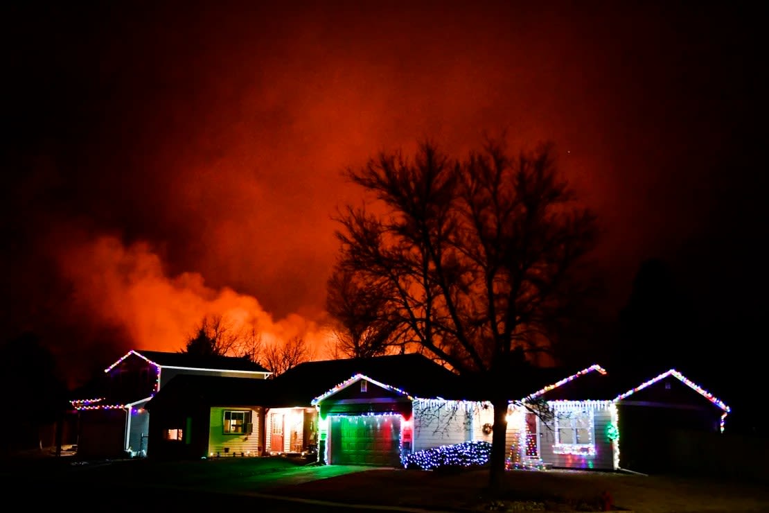 Las luces de Navidad adornan una casa mientras el incendio de Marshall arrasa en el fondo el 30 de diciembre de 2021, en Louisville, Colorado.