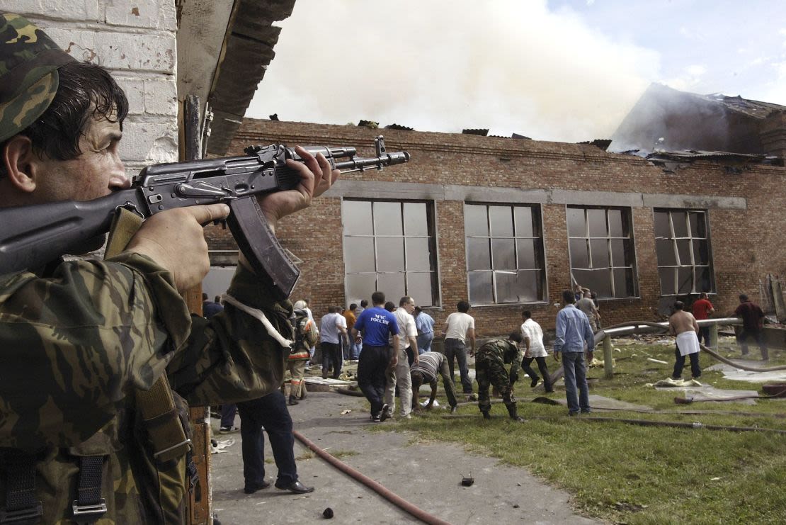 Un soldado cubre el tejado mientras unos voluntarios inspeccionan la zona tras el asalto de las fuerzas especiales a una escuela tomada por los separatistas chechenos el 3 de septiembre de 2004 en la ciudad de Beslán, Rusia. Crédito: Oleg Nikishin/Getty Images