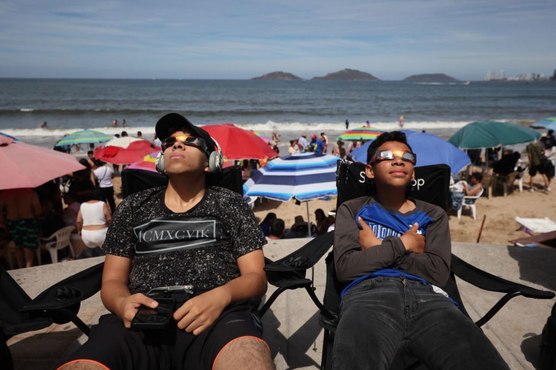 Dos niños llevan gafas de sol para disfrutar del eclipse desde la playa en Mazatlán, México.