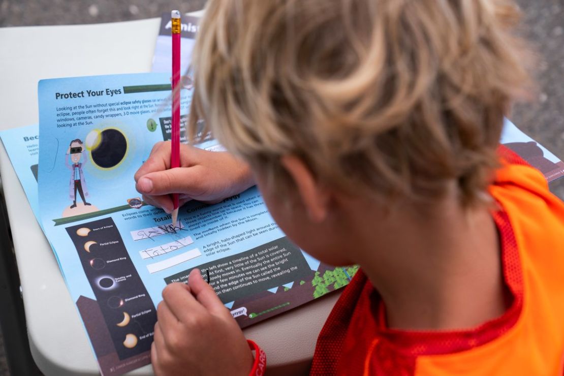 Un niño rellena un libro de actividades Junior Ranger durante una fiesta de observación del eclipse en el Área Recreativa Nacional Amistad en Del Río.