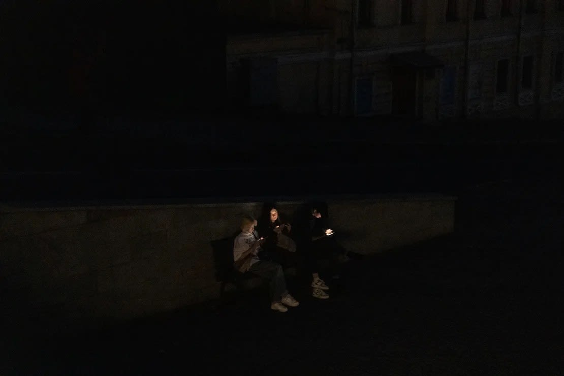 La gente se sienta en un banco mientras revisan sus teléfonos inteligentes en una calle durante un apagón tras los ataques rusos en Kharkiv, el 8 de abril de 2024 . (Foto: Roman Pilipey/AFP/Getty Images).