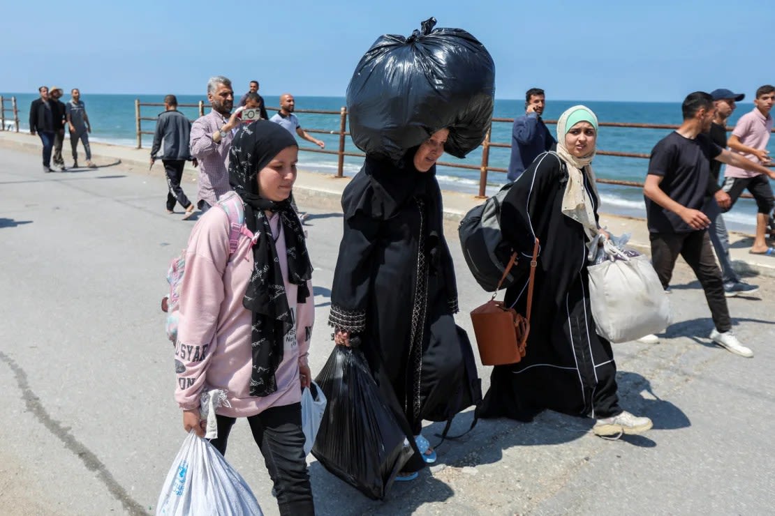 Um Mohammad (centro) camina por la carretera con una pesada bolsa en la cabeza y otras dos en brazos mientras se dirige hacia el norte de Gaza el 14 de abril de 2024. Crédito: Ramadán Abed/Reuters.