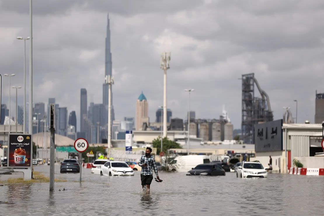 Un hombre camina sobre el agua de las inundaciones provocadas por las fuertes lluvias, con la torre Burj Khalifa visible al fondo, en Dubai, Emiratos Árabes Unidos, 17 de abril de 2024.