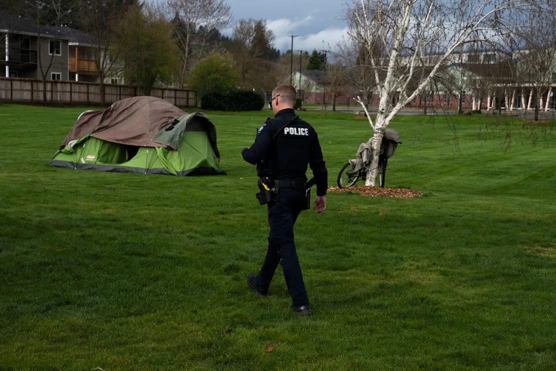 Un oficial de la Policía de Grants Pass investiga a una persona sin hogar después de que sus familiares solicitaron un control de asistencia social en Fruitdale Park, el 23 de marzo de 2024. (Foto: Jenny Kane/AP/Archivo).