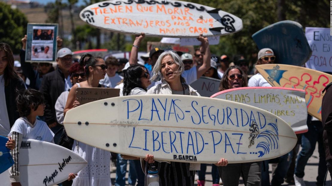 Una mujer sostiene una tabla de surf que dice "Playas, Seguridad, Libertad, Paz" junto a miembros de la comunidad de surfistas que protestaban contra la inseguridad después de que dos surfistas australianos y un estadounidense desaparecieran durante un viaje de surf, en Ensenada, Baja California, México, el 5 de mayo.