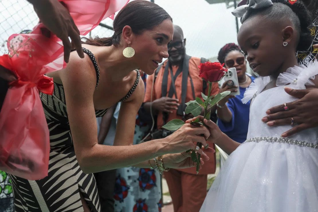 Meghan, duquesa de Sussex, recibe flores de una niña a su llegada con el príncipe Harry, duque de Sussex, de Gran Bretaña, para un partido de voleibol en Nigeria Unconquered, una organización benéfica local que apoya a miembros del servicio heridos, lesionados o enfermos, en Abuja el 11 de mayo de 2024. Crédito: Kola Sulaimon/AFP/Getty Images.