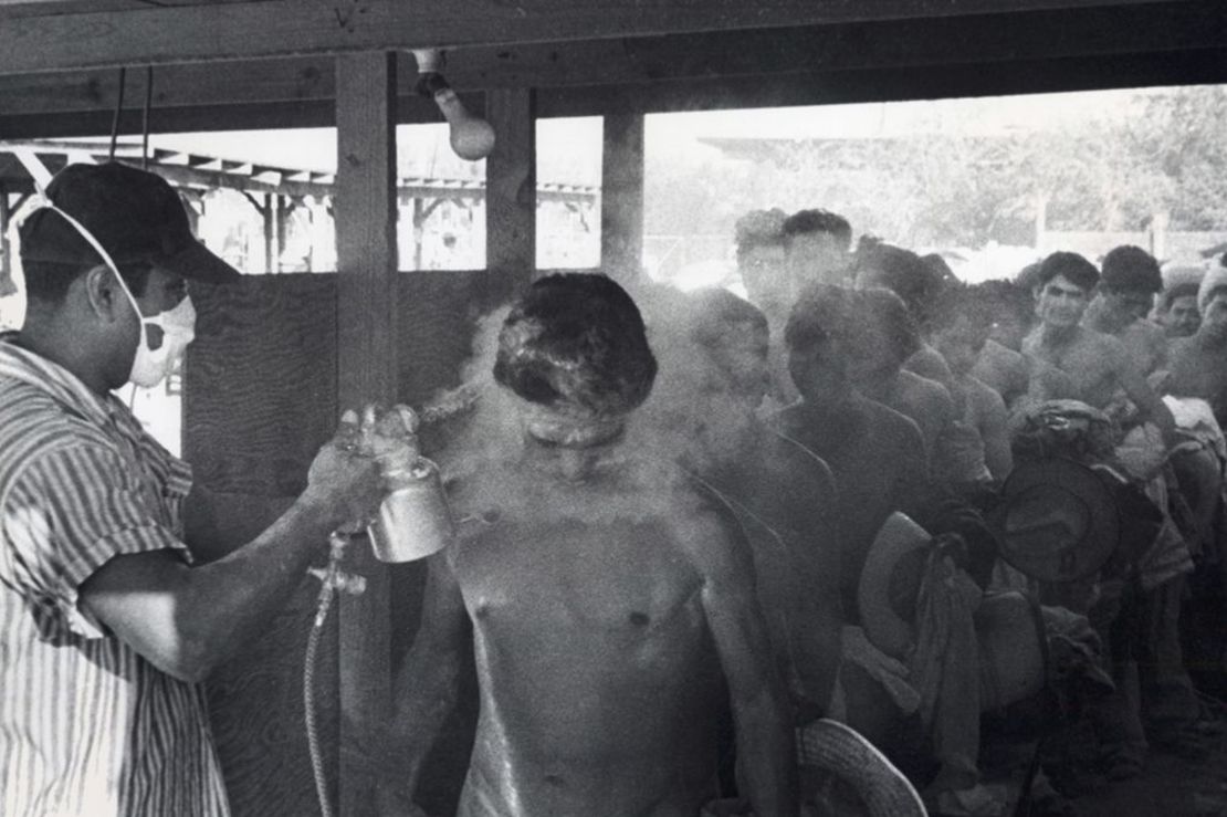 Esta foto tomada en Hidalgo, Texas, en 1956 muestra a un trabajador enmascarado rociando braceros con DDT mientras otros esperan en fila. Crédito: Oficina de Historia y Biblioteca del USCIS/Departamento de Seguridad Nacional