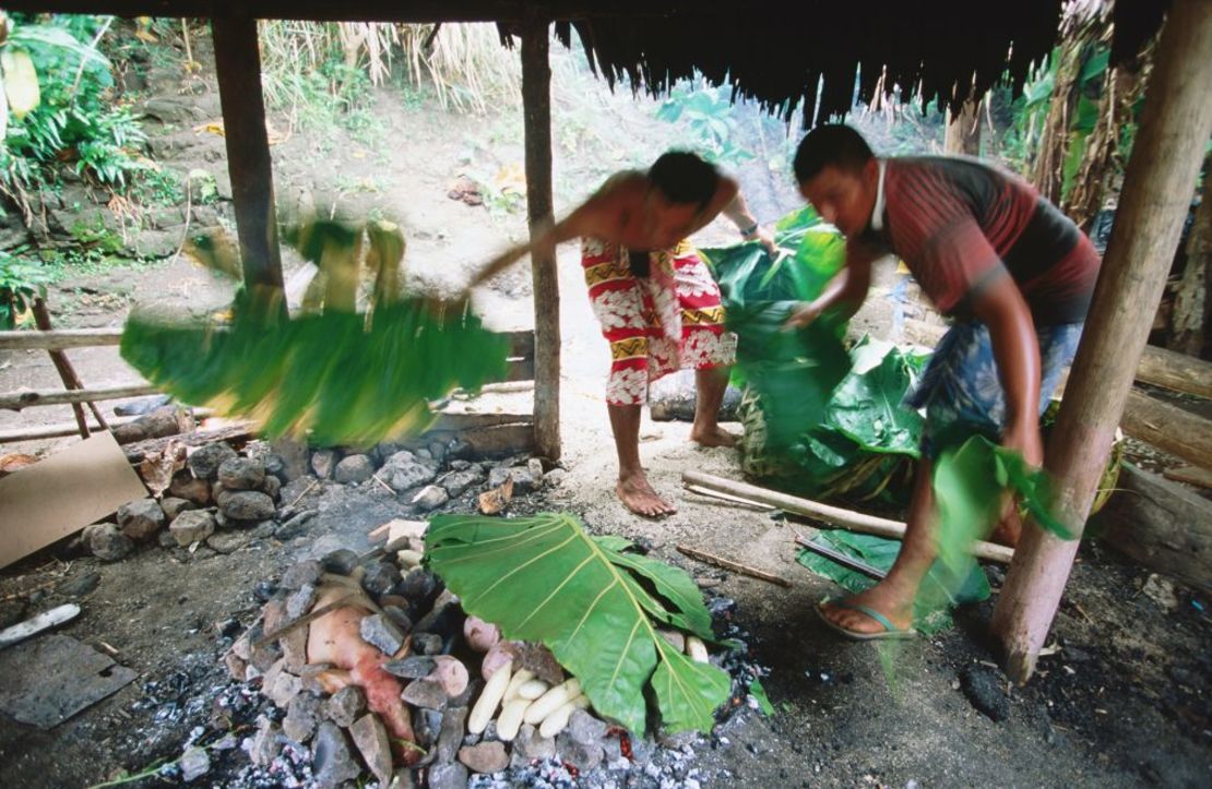 Hombres cubren con hojas el umu, la versión samoana de la barbacoa. Crédito: Holger Leue/The Image Bank Unreleased/Getty Images