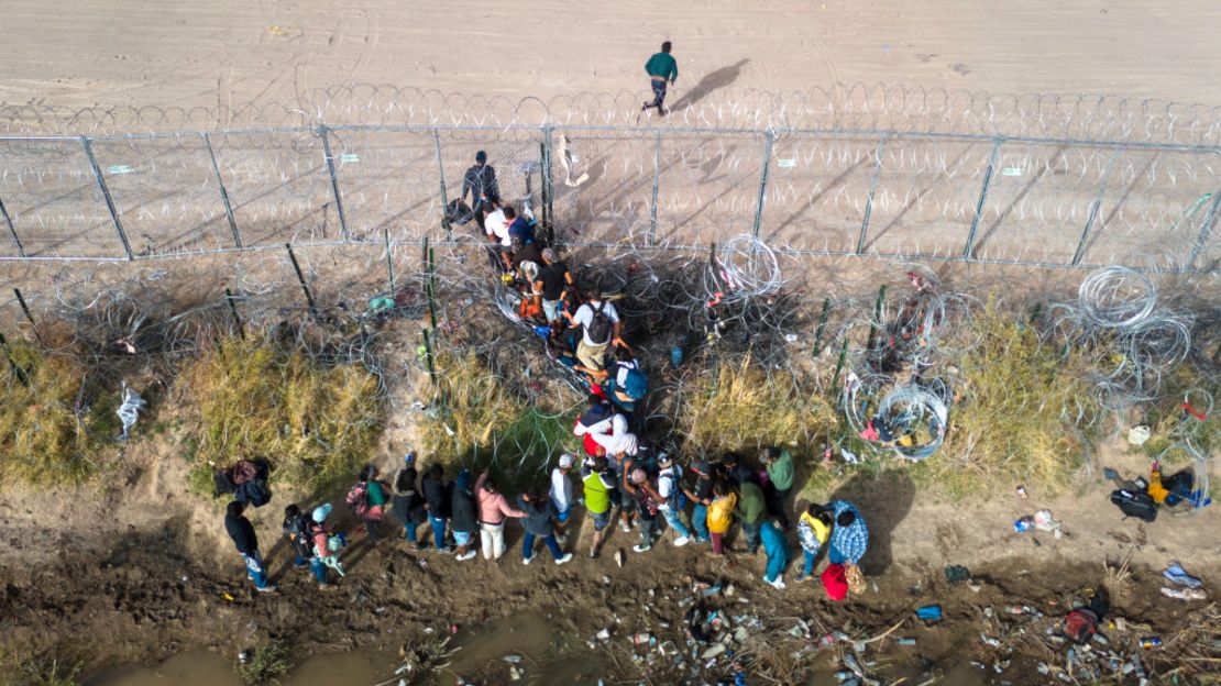 En una vista aérea, inmigrantes pasan a través de rollos de alambre de púas en la frontera entre Estados Unidos y México el 13 de marzo de 2024 en El Paso, Texas.