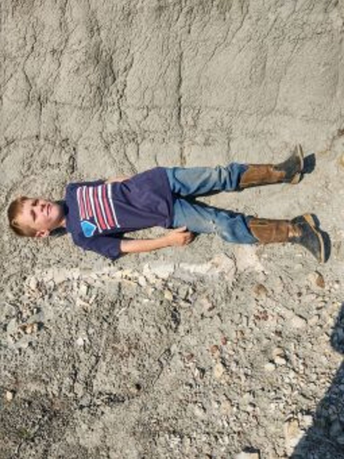 Liam Fisher posa recostado junto al descubrimiento del dinosaurio. Su padre envió esta imagen a Lyson, un antiguo compañero de clase, que preparó el terreno para la excavación del fósil. Crédito: Cortesía del Museo de Naturaleza y Ciencia de Denver