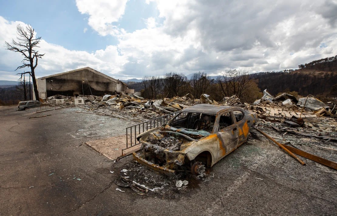 En la fotografía se muestra un automóvil carbonizado y los restos del Swiss Chalet Hotel después de ser destruidos por el incendio de South Fork en el pueblo de montaña de Ruidoso, Nuevo México, el sábado.