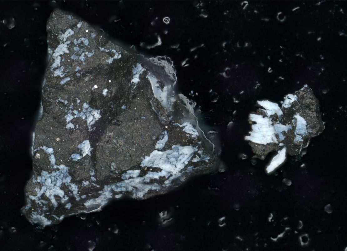 Una imagen de microscopio muestra una partícula oscura de Bennu, de aproximadamente un milímetro de longitud, con una costra de fosfato brillante. Crédito: Lauretta & Connolly et al. (2024)/Meteoritics & Planetary Science