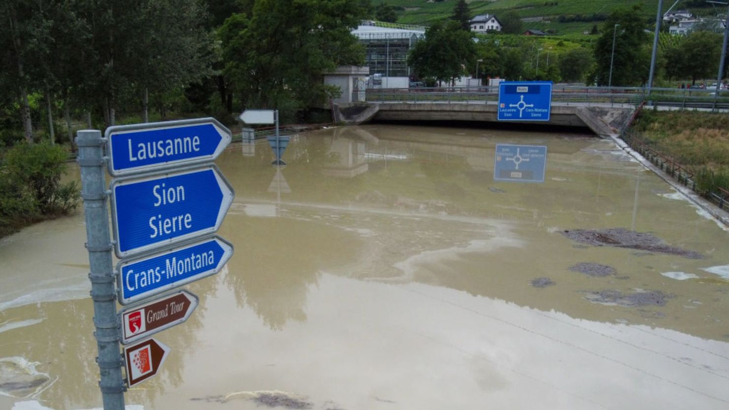 Una fotografía tomada el 30 de junio de 2024 muestra señales de tráfico sobre una carretera inundada cerca de Sierre, Suiza.