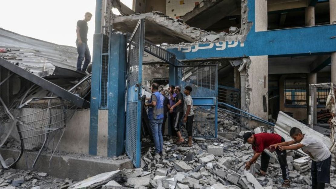 Palestinos y trabajadores de la ONU examinan las tiendas y refugios improvisados destruidos tras el ataque israelí contra una escuela del Organismo de Obras Públicas y Socorro de las Naciones Unidas para los Refugiados de Palestina en el Cercano Oriente (OOPS), que causó numerosos muertos y heridos en el campo de refugiados de Nuseirat de Deir al-Balah, Gaza, el 15 de julio de 2024.