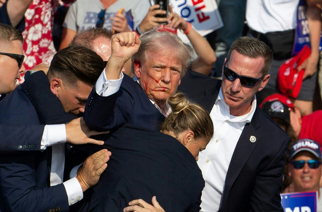 TOPSHOT - Republican candidate Donald Trump is seen with blood on his face surrounded by secret service agents as he is taken off the stage at a campaign event at Butler Farm Show Inc. in Butler, Pennsylvania, July 13, 2024. Donald Trump was hit in the ear in an apparent assassination attempt by a gunman at a campaign rally on Saturday, in a chaotic and shocking incident that will fuel fears of instability ahead of the 2024 US presidential election. The 78-year-old former president was rushed off stage with blood smeared across his face after the shooting in Butler, Pennsylvania, while the gunman and a bystander were killed and two spectators critically injured. (Photo by Rebecca DROKE / AFP)