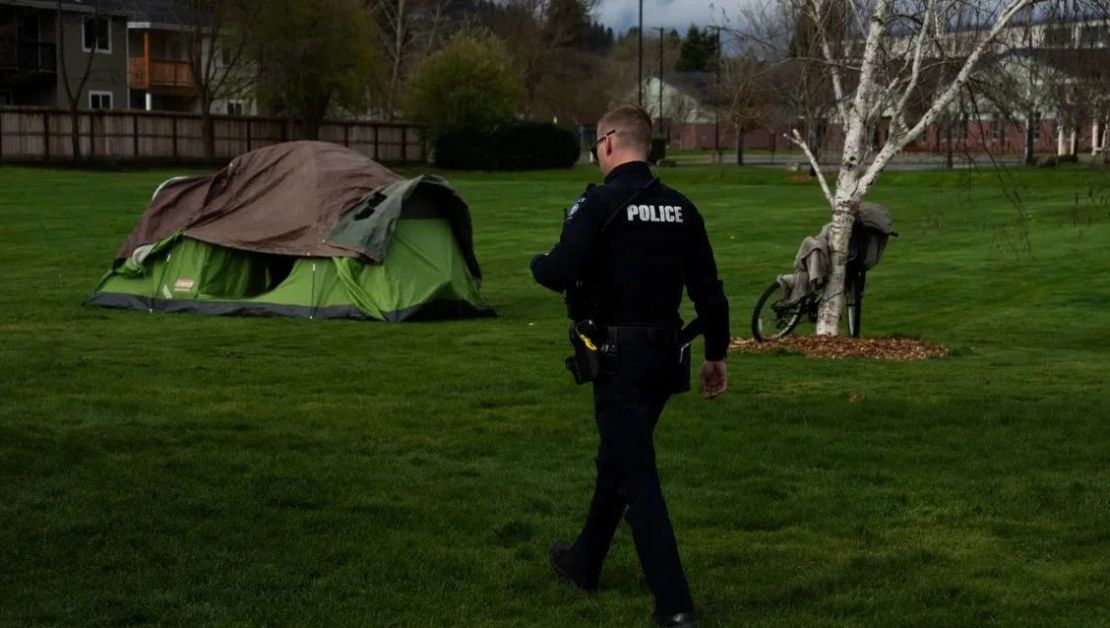 Un agente de policía camina para controlar a una persona sin hogar el sábado 23 de marzo de 2024 en Grants Pass, Oregón. Jenny Kane/AP