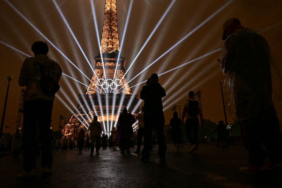 Los asistentes toman fotografías de la Torre Eiffel mientras los láseres iluminan el cielo durante la ceremonia de apertura de los Juegos Olímpicos de París 2024. Martín Bernetti/AFP/Getty Images.