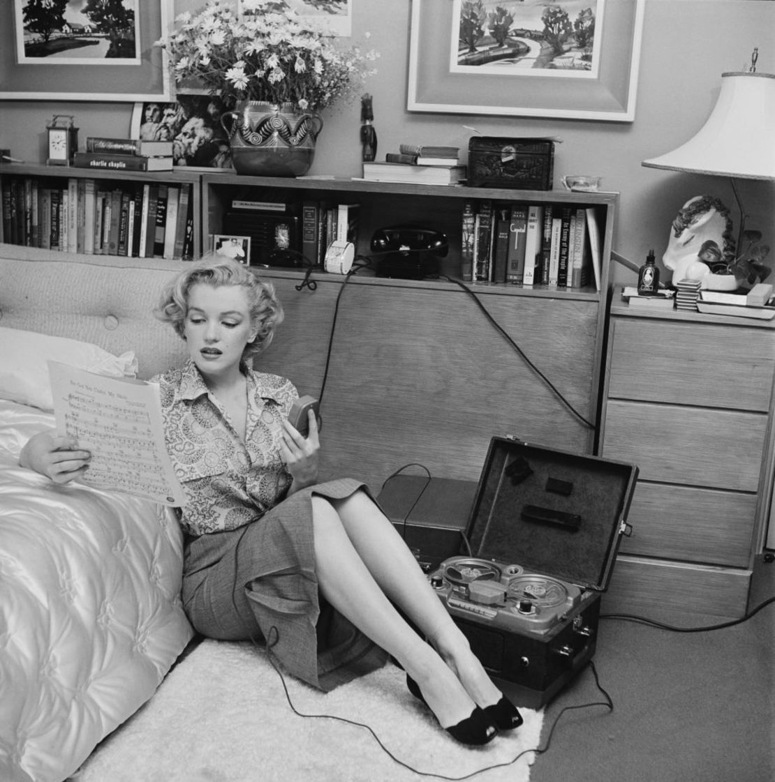 La actriz estadounidense Marilyn Monroe (1926-1962) leyendo partituras mientras está sentada en el piso de un dormitorio con un reproductor de cintas a un costado, hacia 1950. Foto de Archive Photos/Getty Images