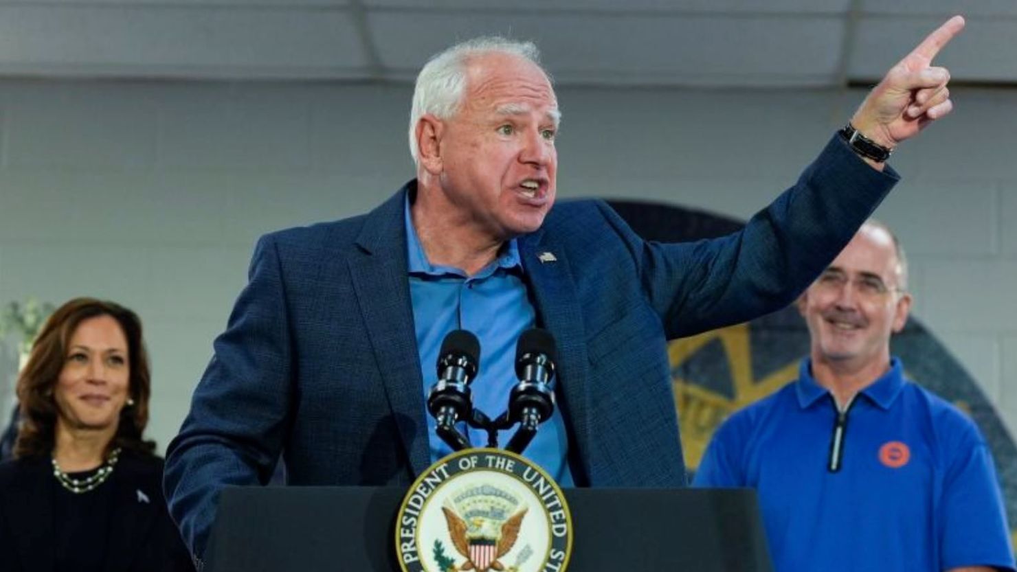 El candidato demócrata a la vicepresidencia, el gobernador de Minnesota Tim Walz (C), habla mientras la candidata demócrata a la presidencia, la vicepresidenta de EE.UU. Kamala Harris (I), y el presidente de U.A.W., Shawn Fain (D), lo observan en un mitin de campaña en United Auto Workers Local 900 el 8 de agosto de 2024 en Wayne, Michigan. Kamala Harris y su recién seleccionada compañera de fórmula, Tim Walz, están haciendo campaña por todo el país esta semana. "