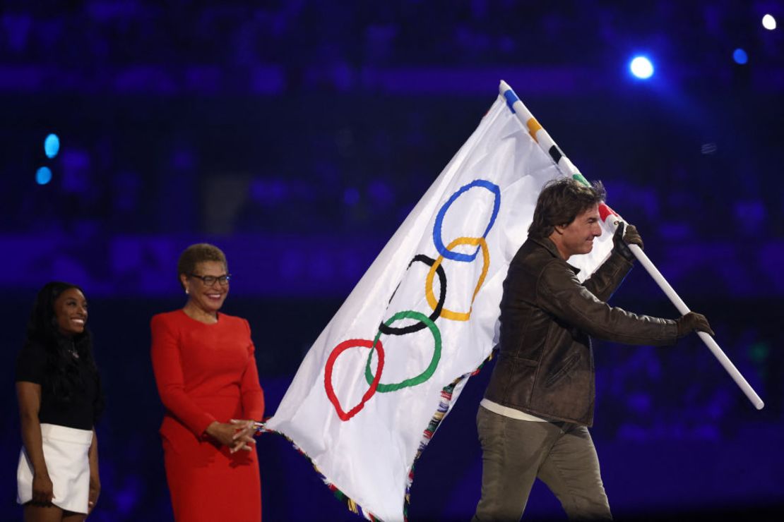 El actor estadounidense Tom Cruise sale con la bandera olímpica frente a la alcaldesa de Los Ángeles, Karen Bass, durante la ceremonia de clausura de los Juegos Olímpicos de París 2024 en el Stade de France. A la izquierda de Bass se encuentra la gimnasta estadounidense Simone Biles. Crédito: FRANCK FIFE/AFP vía Getty Images