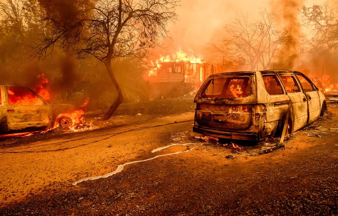 El metal fundido de un automóvil quemado serpentea por la carretera mientras las llamas envuelven una casa durante el incendio de Thompson en Oroville, California, el 2 de julio.