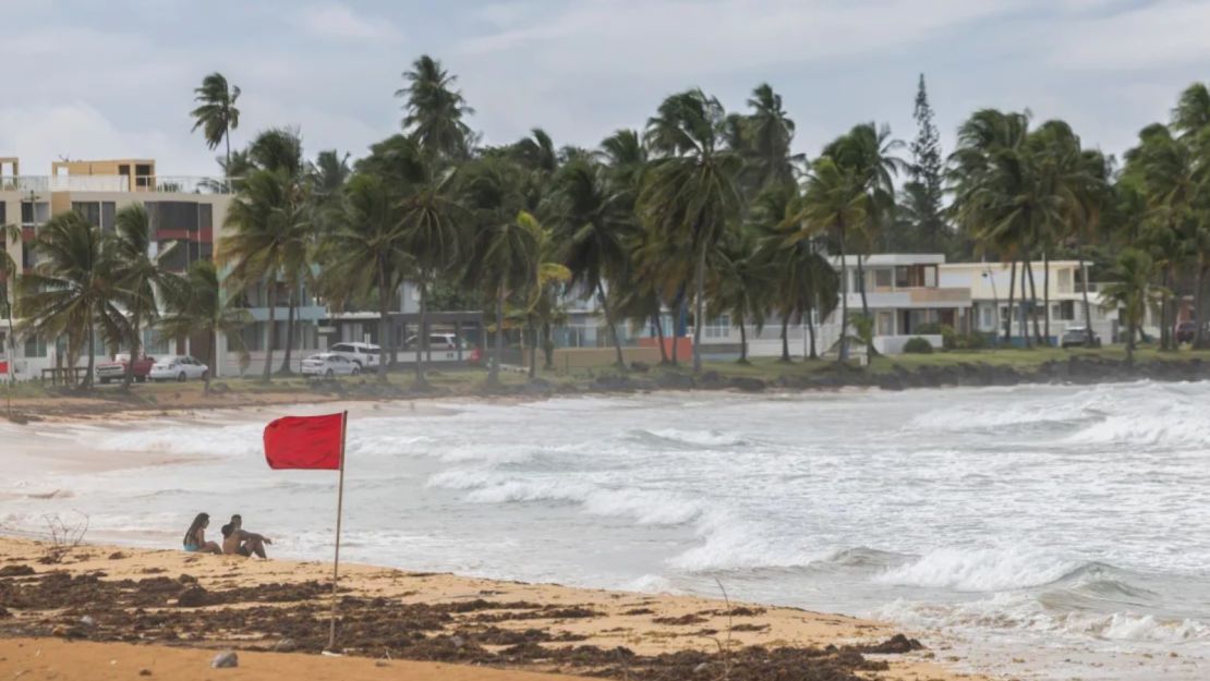 Turistas se sientan en la playa de La Pared mientras la Tormenta Tropical Ernesto agita las olas cerca de Luquillo, Puerto Rico, el martes.