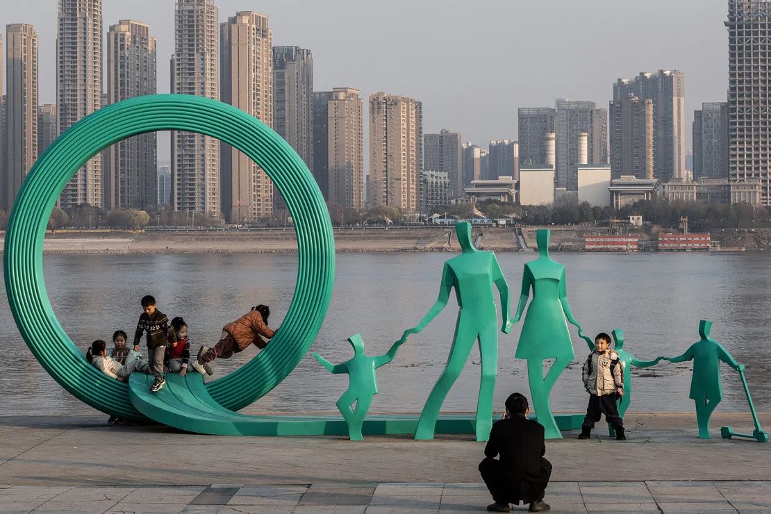 La gente posa junto a una estatua recientemente renovada con dos niños más agregados al diseño original de familia de un solo hijo en el Parque Hankou, Wuhan, en la provincia china de Hubei, el 5 de enero de 2024.