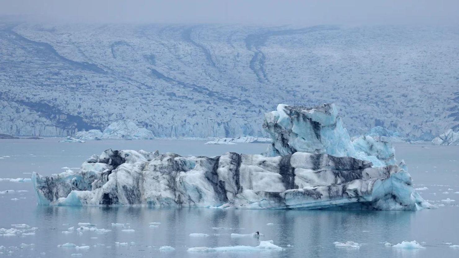 Un iceberg que se desprendió del glaciar Breidamerkurjokull en retroceso, que se ve detrás, flota en el lago Jokulsarlon el 15 de agosto de 2021 cerca de Hof, Islandia.