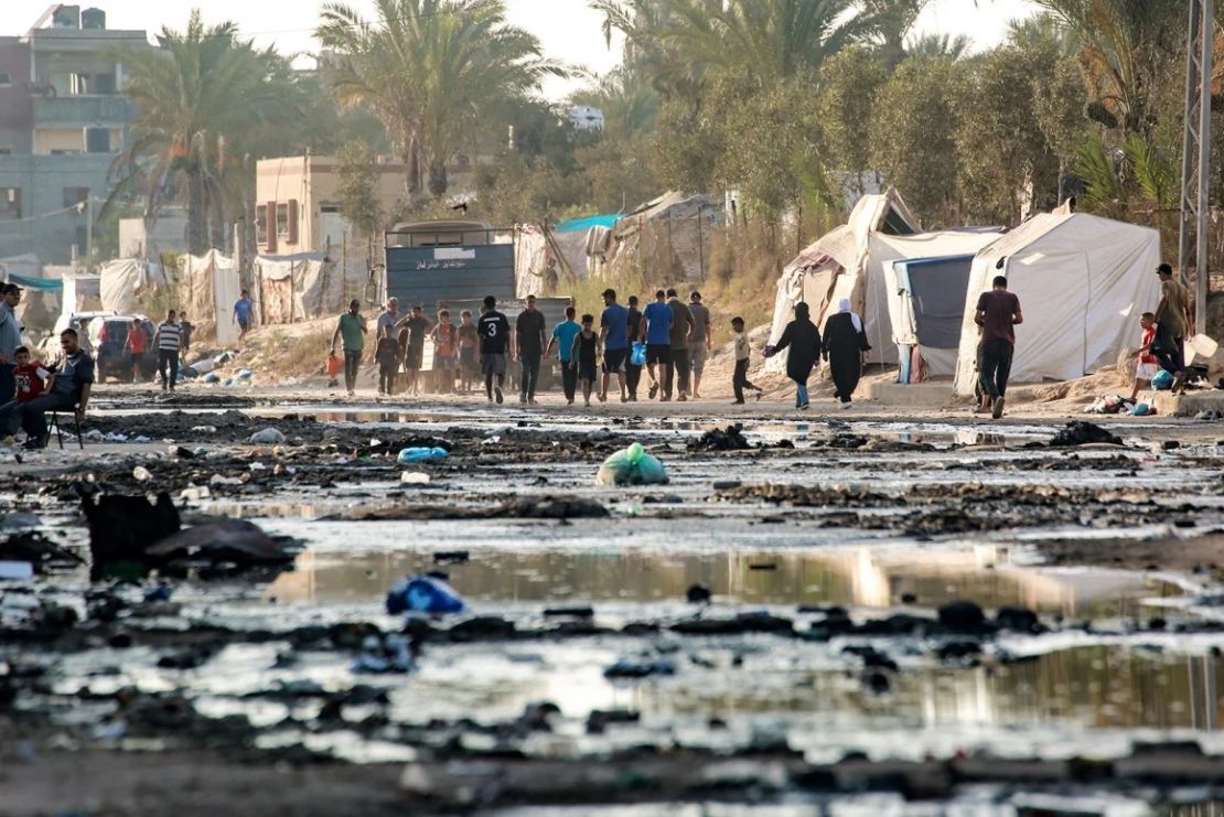 Palestinos desplazados caminan por una calle cubierta de aguas residuales estancadas en Deir el-Balah, en el centro de Gaza, el 19 de julio. Un alto el fuego permitiría un momento de alivio para los habitantes de Gaza, después de casi un año de ataques israelíes. Crédito: Bashar Taleb/AFP/Getty Images.