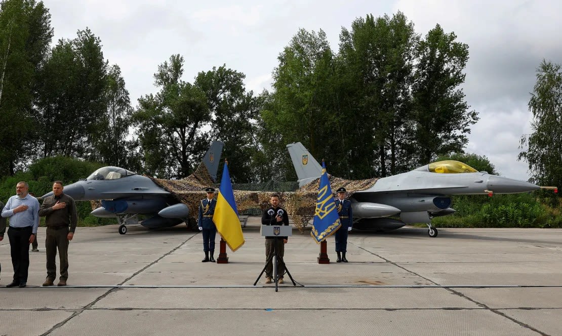 El presidente de Ucrania, Volodymyr Zelenskiy, canta el himno nacional junto a aviones de combate F-16 durante el Día de las Fuerzas Aéreas Ucranianas en un lugar no revelado, Ucrania, el 4 de agosto de 2024.