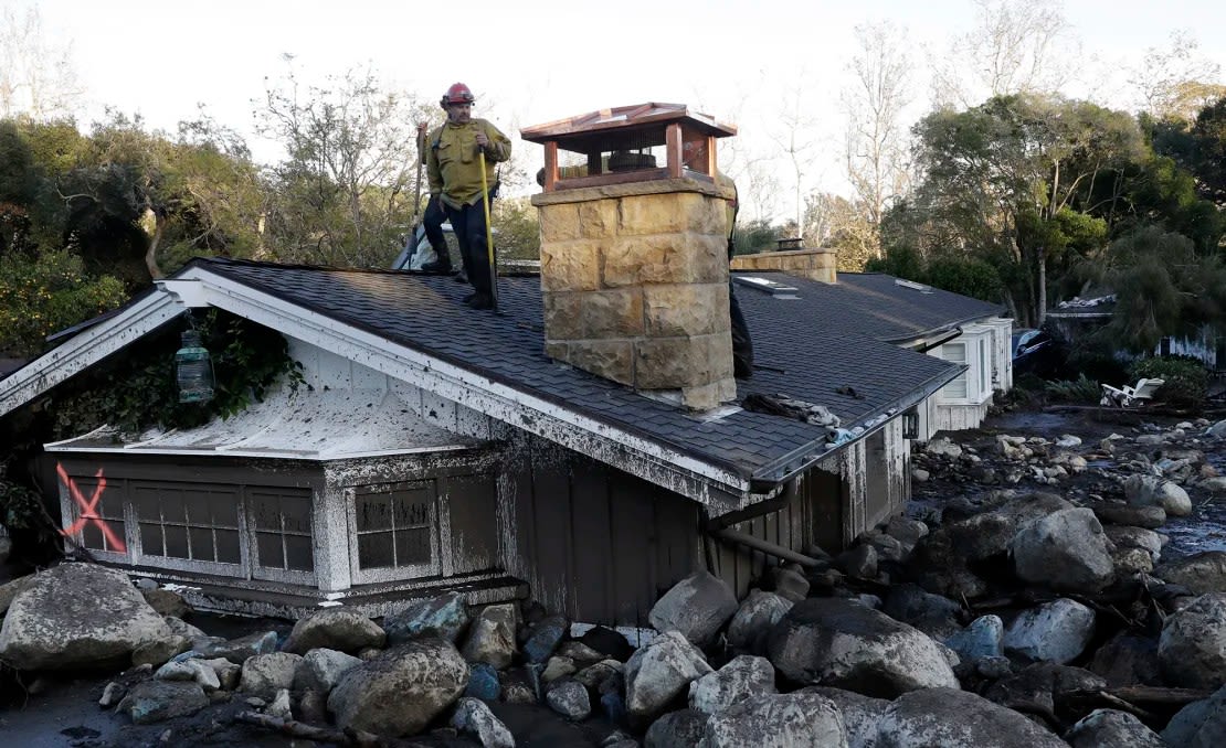 Un bombero se para en el tejado de una casa sumergida en barro y rocas tras un deslizamiento de tierra en Montecito, California, en 2018.