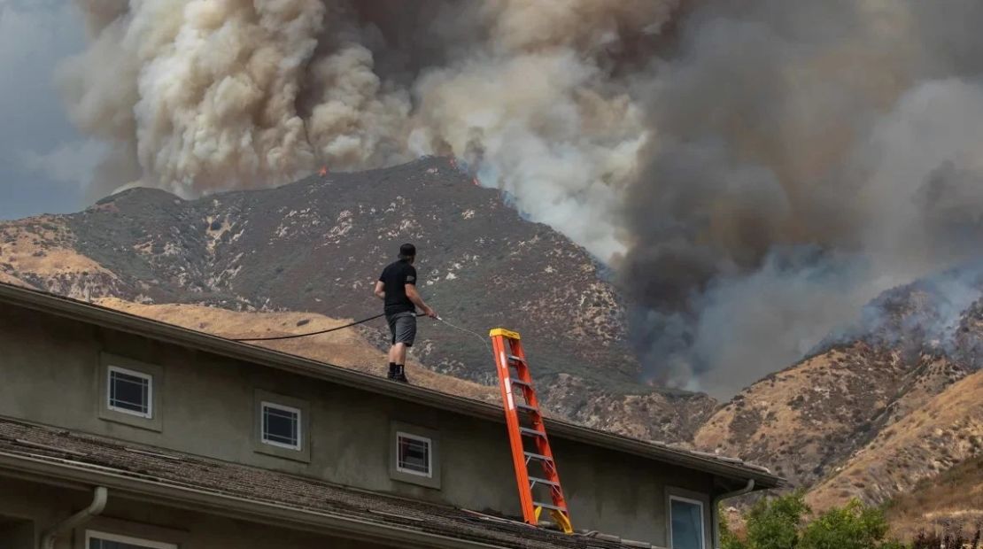 Un hombre riega el techo de su casa mientras el incendio arde en las estribaciones de las montañas de San Bernardino, lo que obliga a evacuaciones. Apu Gomes/Getty Images