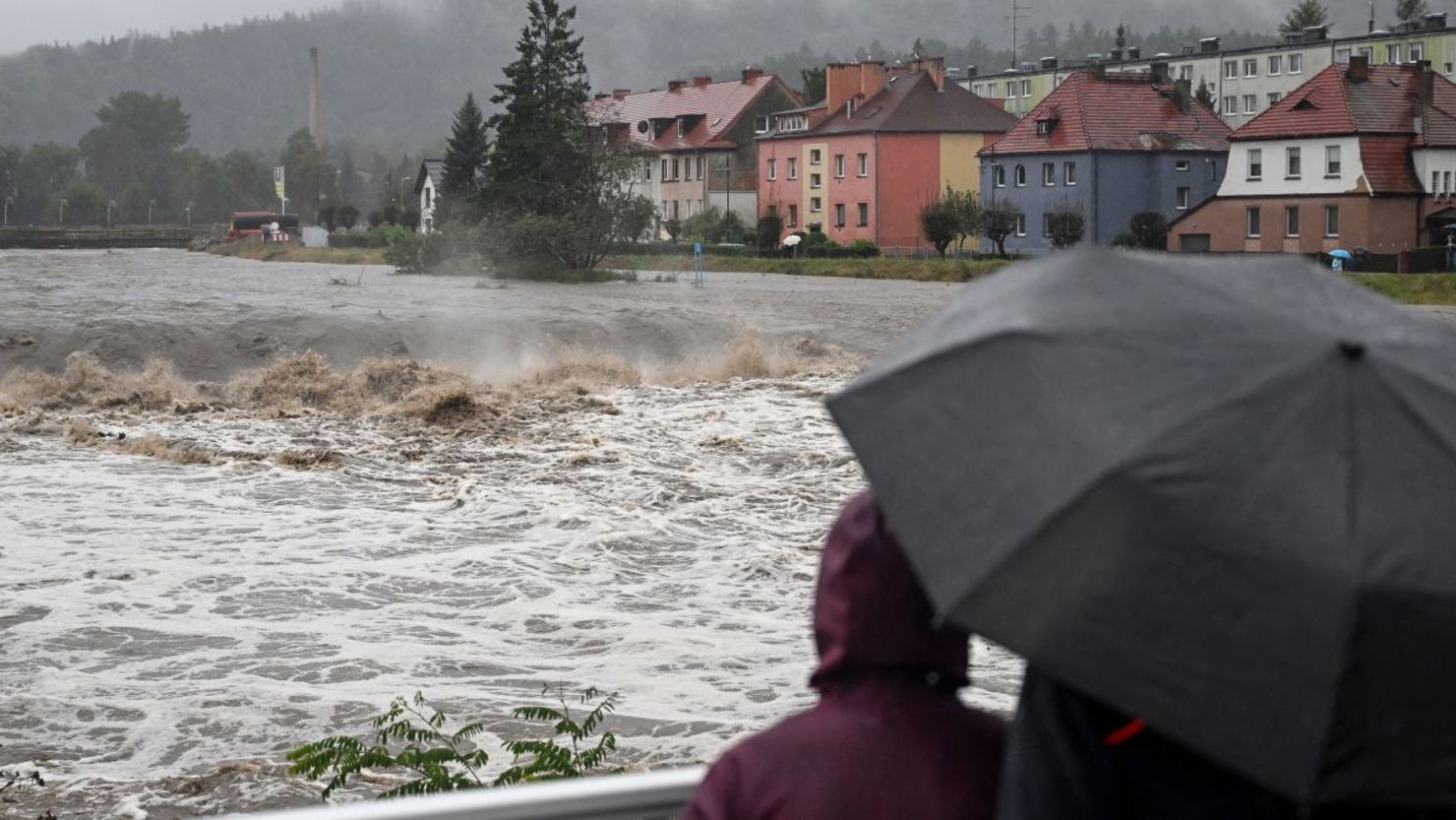 Personas se refugian de la lluvia bajo paraguas mientras cruzan un puente sobre el río Biala en Glucholazy, en el sur de Polonia, el sábado.