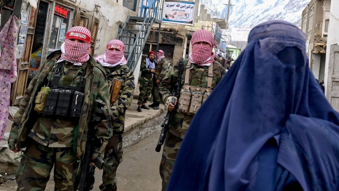 Personal de seguridad talibán vigila mientras una mujer vestida con burqa camina por un mercado en el distrito de Baharak, provincia de Badakhshan, Afganistán, el 26 de febrero de 2024.