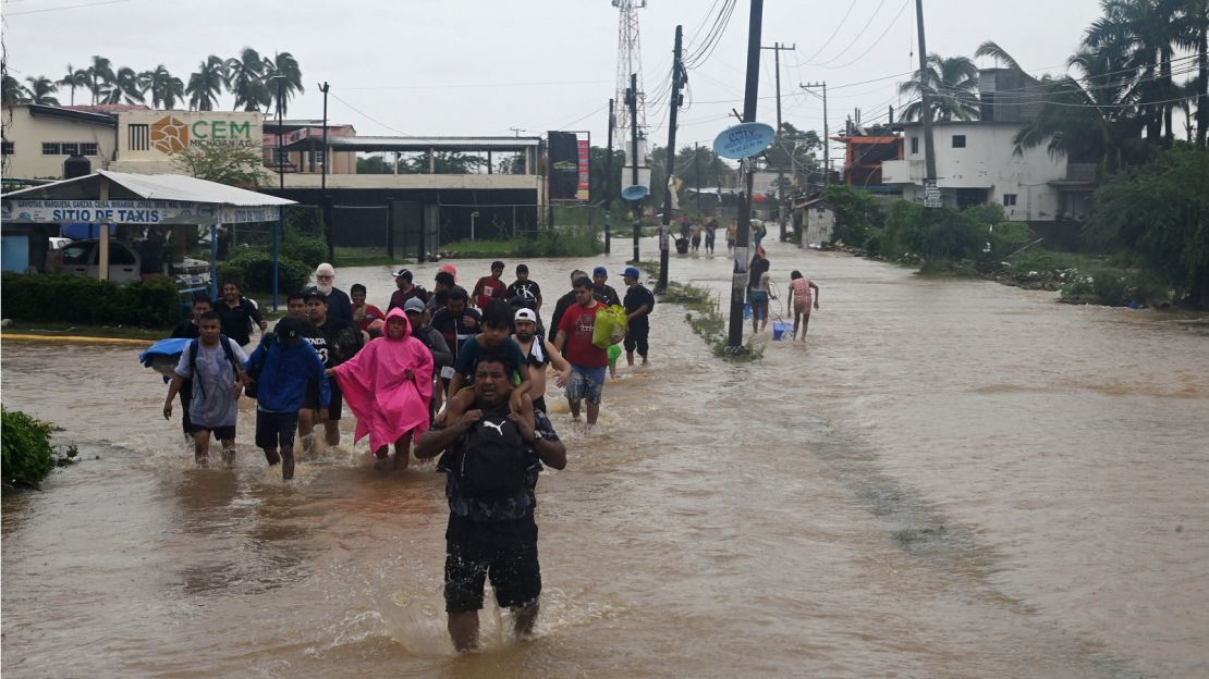 Varias personas caminan por una calle inundada en dirección a un refugio tras el paso del huracán John en Acapulco, estado de Guerrero.