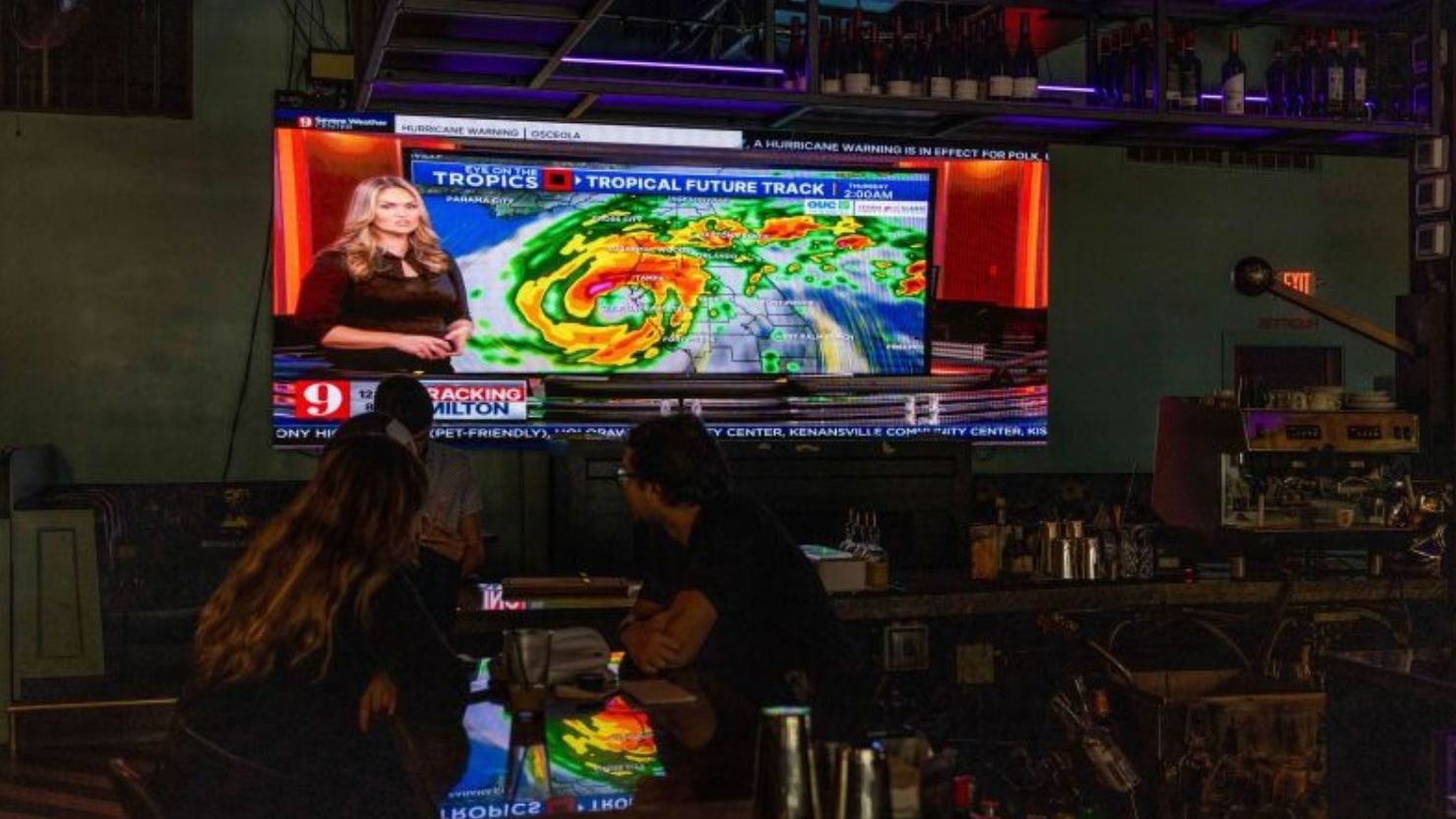 Personas ven una pantalla de televisión en un bar que muestra el canal de noticias local, mientras la comunidad se prepara para el huracán Milton en Orlando, Florida, el 8 de octubre de 2024.
