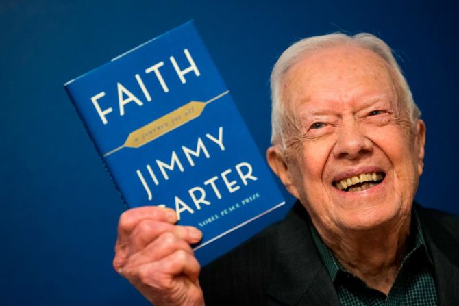 Carter levanta una copia de su nuevo libro "Faith: A Journey For All" en un evento de firma de libros en Nueva York en marzo de 2018.