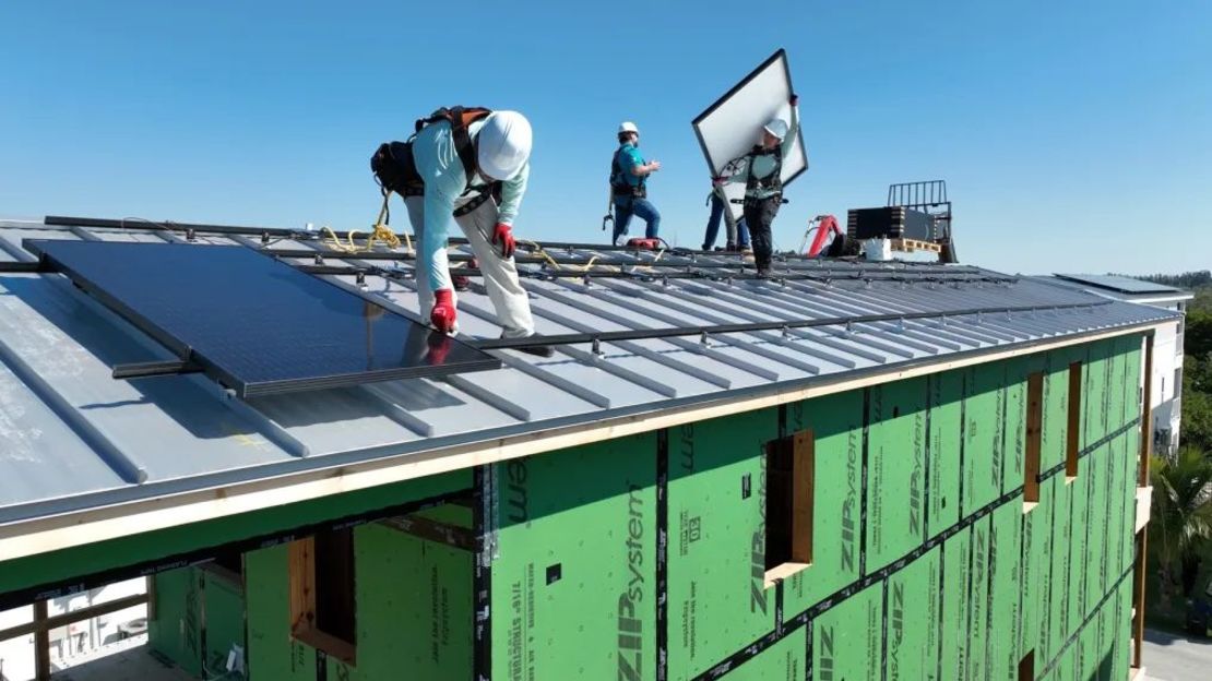 Trabajadores fijan paneles solares a las juntas verticales elevadas de los tejados para evitar que salgan volando durante violentas tormentas en abril de 2024.