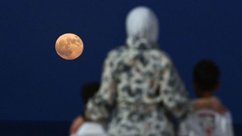 Una mujer con dos niños observa la superluna llena de septiembre (la primera del año) que se eleva sobre las aguas del golfo, frente a la costa de la ciudad de Kuwait, el 18 de septiembre de 2024.