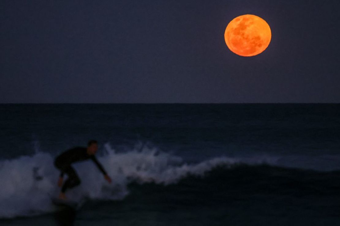 Un surfista toma una ola mientras la superluna de septiembre (la primera del año) se eleva detrás en la playa de Manly, en Sydney, Australia, el 18 de septiembre de 2024.