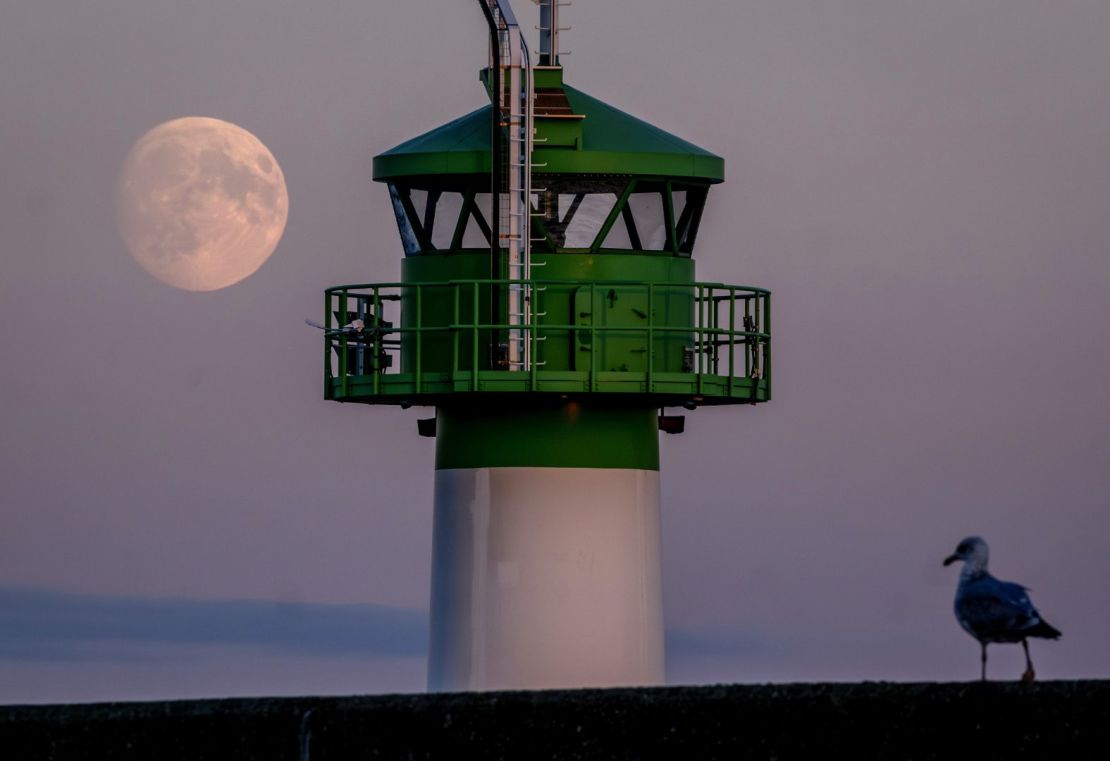 La luna se eleva detrás del faro en el puerto de Travemuende, en el norte de Alemania, este martes 15 de octubre.