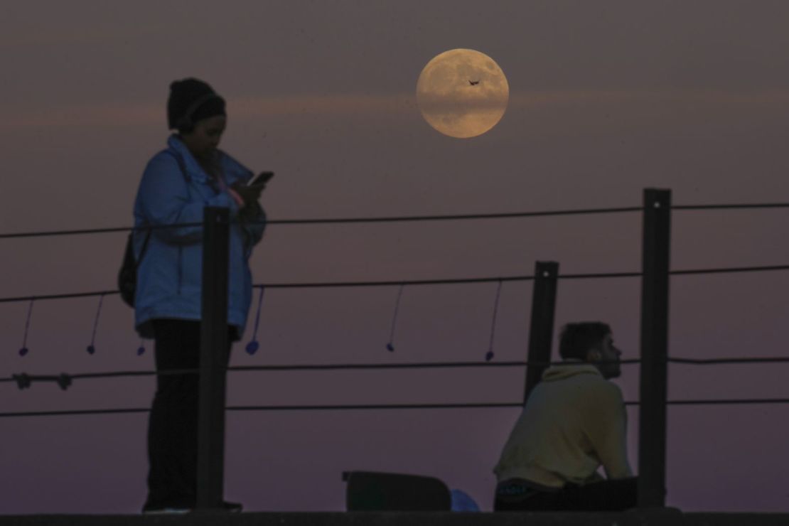 Un avión cruza la superluna mientras la gente la observa elevarse sobre el lago Michigan en Chicago, este miércoles.