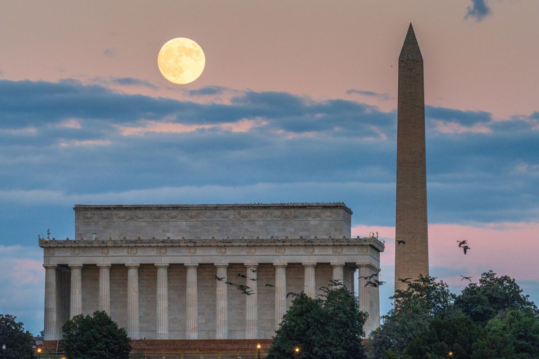 La luna se eleva detrás del Monumento a Lincoln y el Monumento a Washington, mientras una bandada de pájaros pasa este miércoles.