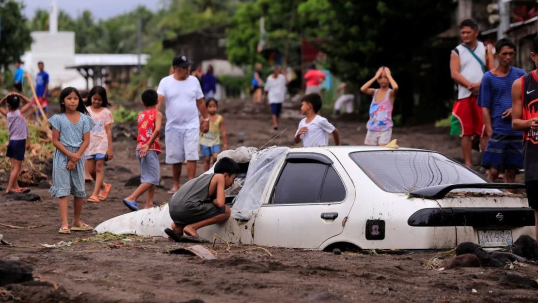 Los residentes miran un automóvil sepultado por ceniza volcánica que cayó en una aldea debido a las intensas lluvias generadas por la tormenta tropical Trami en una aldea del municipio de Guinobatan, provincia de Albay, al sur de Manila, Filipinas, el 23 de octubre de 2024.