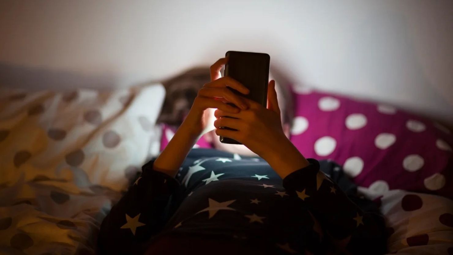 Una niña yace en la cama por la noche, mirando su teléfono.