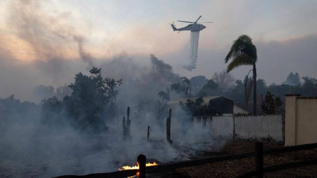 Un helicóptero arroja agua sobre una estructura en llamas durante un rápido incendio forestal en Moorpark, California.