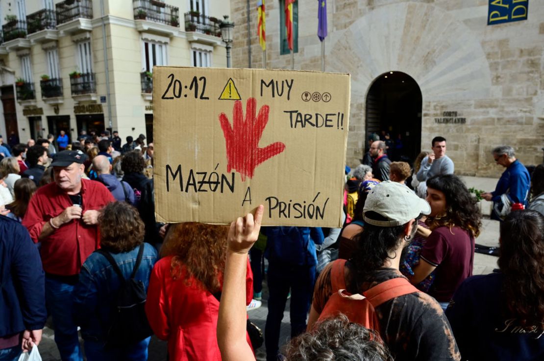 Una persona levanta un cartel que dice "20:12 ¡muy tarde! Mazón a prisión" mientras decenas de manifestantes se reúnen frente al parlamento regional de Valencia, el 15 de noviembre de 2024.