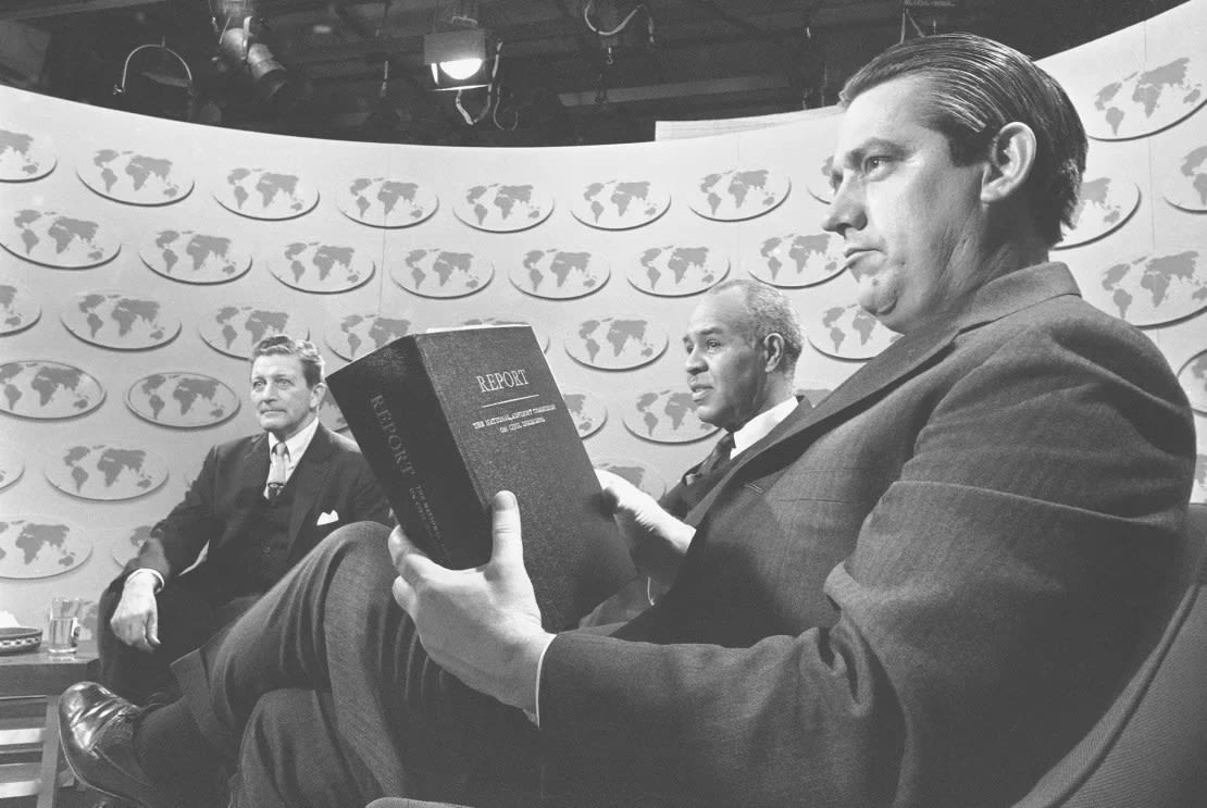 El senador de Oklahoma Fred R. Harris sostiene una copia del informe de la Comisión Asesora Nacional sobre Desórdenes Civiles mientras él y otros dos miembros de la comisión debaten el estudio en el programa de radio y televisión "Temas y respuestas", el 3 de marzo de 1968.